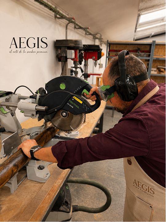 Artesano cortando y ajustando piezas de madera para un parasol AEGIS™ en el taller de fabricación, combinando precisión técnica, materiales nobles y trabajo artesanal.
